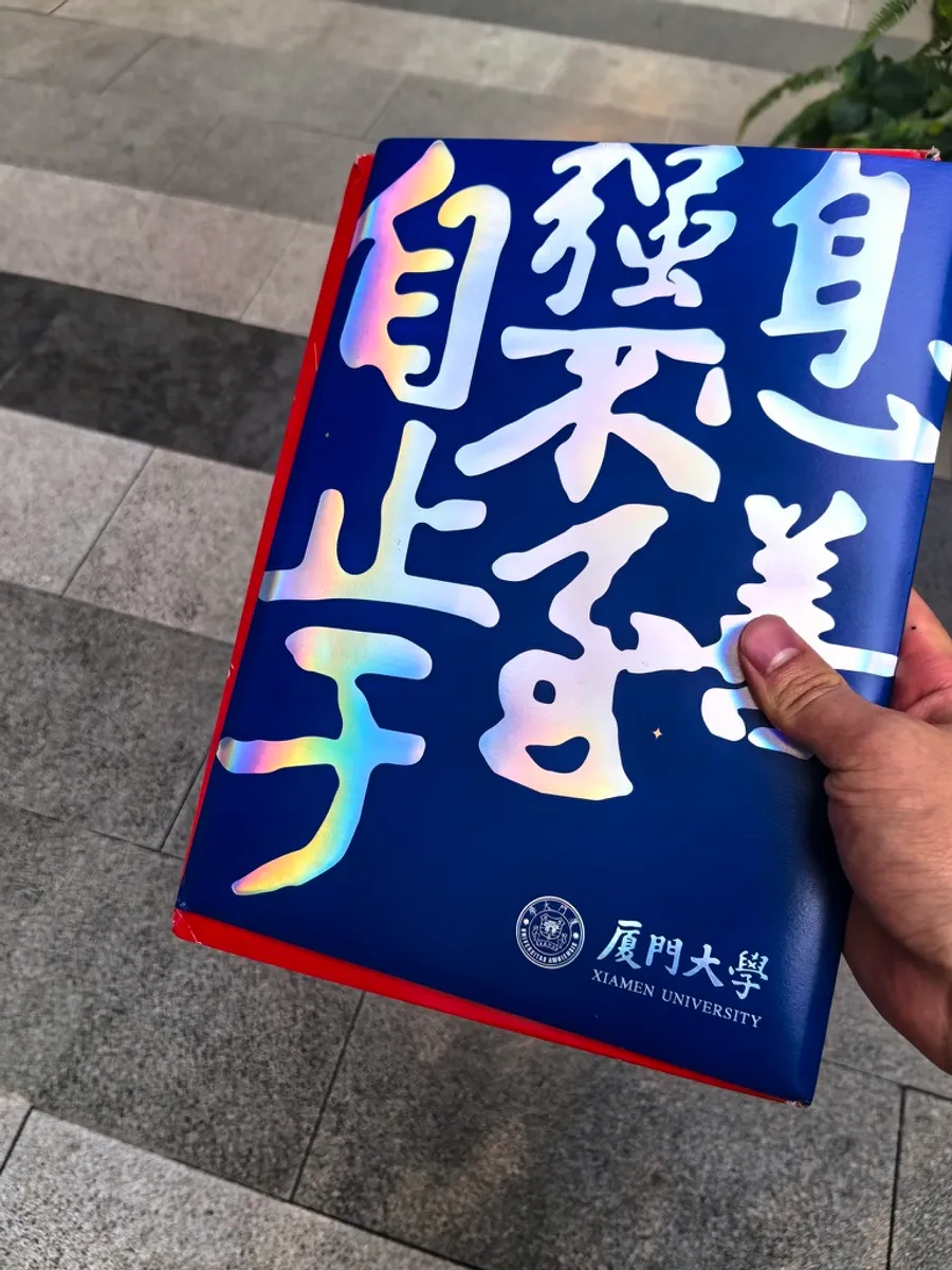 Holding the navy Xiamen University admission box, its cover stamped with holographic Chinese characters.