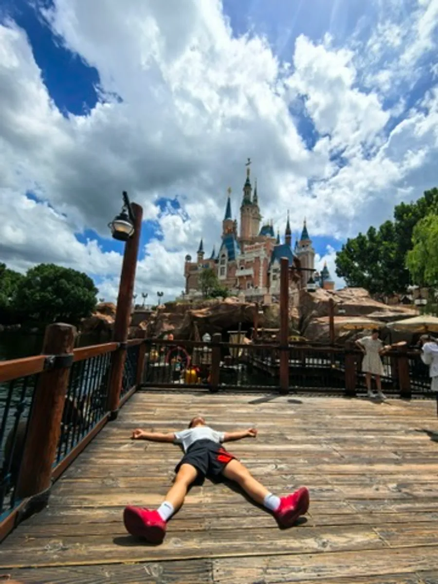 Flat on my back, arms and legs spread, on a wooden bridge in front of the Shanghai Disneyland castle.